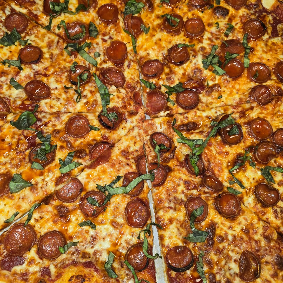 A whole pepperoni pizza, cut into slices, topped with fresh basil and melted cheese.