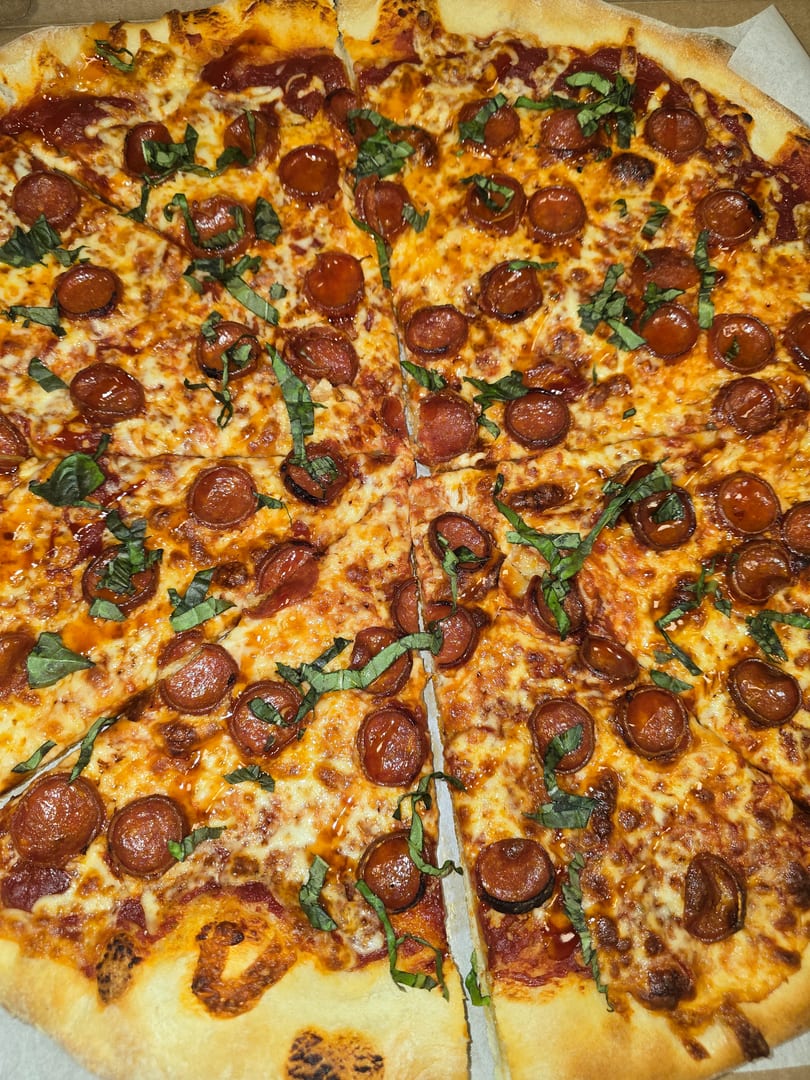 A whole pepperoni pizza, cut into slices, topped with fresh basil and melted cheese.