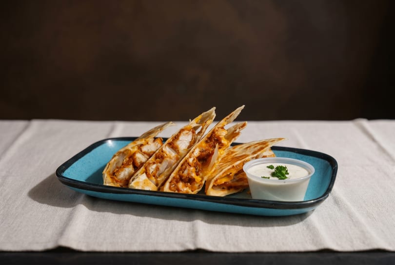 Chicken quesadillas with melted cheese and a side of ranch dressing on a blue plate.